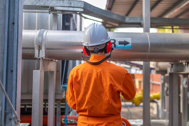 Ingeniero joven que trabaja en una gran fábrica Técnico con uniforme de protección y con casco duro comprobando la temperatura en las tuberías