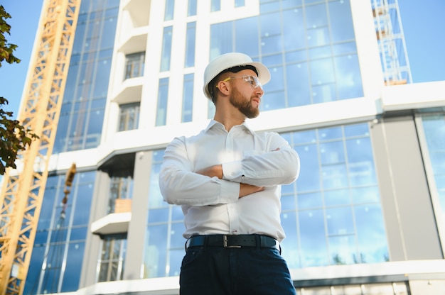 Ingeniero junto a la construcción de grúas. Concepto - gran proyecto de construcción. El arquitecto dirige el proceso de construcción. Dibujos y tableta en las manos.