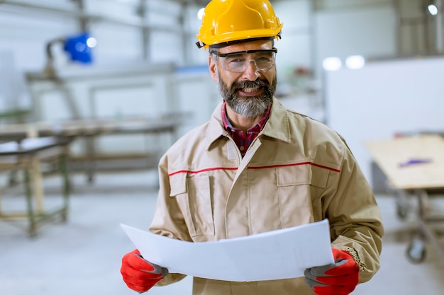 Ingeniero maduro hermoso que mira plan en la fábrica