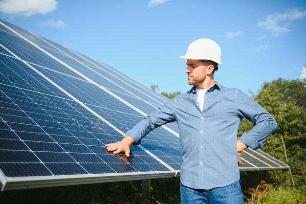 Ingeniero masculino en un casco de pie cerca de los paneles solares mirando hacia arriba Generación de energía ecológica verde Concepto de desarrollo de la estación solar Construcción de viviendas