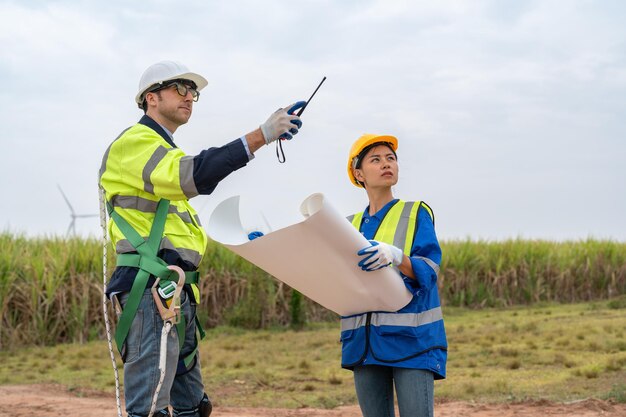 Foto ingeniero masculino y femenino con un plano y discutiendo la inspección de la turbina eólica en una granja eólica