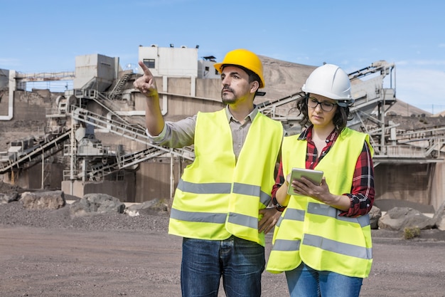 Ingeniero masculino serio apuntando hacia afuera y arquitecta revisando el borrador en la tableta mientras se reúnen en el sitio de construcción industrial