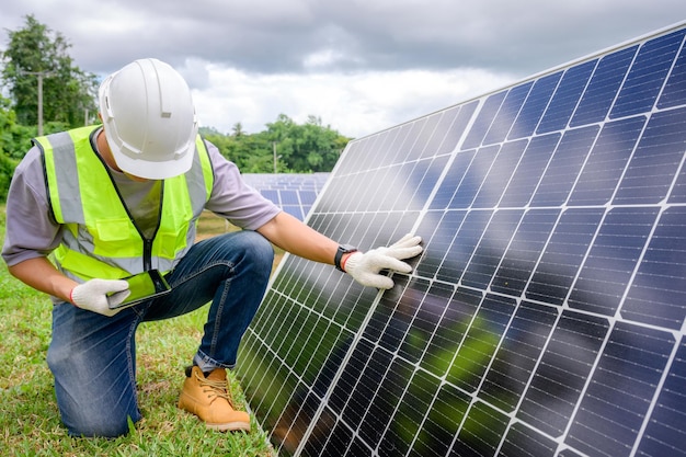 Un ingeniero masculino con un sombrero duro blanco sostiene una tableta para inspeccionar paneles solares en centrales fotovoltaicas que trabajan en el almacenamiento de energía solar industrial