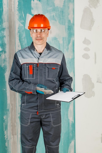 Un ingeniero masculino, un trabajador de la construcción con casco protector y anteojos, escribe en una tableta El concepto de renovación y construcción