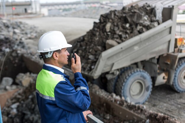 Ingeniero de minas en uniforme supervisa la descarga de dumpers