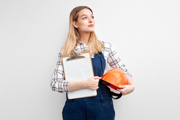 Ingeniero de la mujer que sostiene la tableta de papel y el casco, vestido con el uniforme del mono del constructor