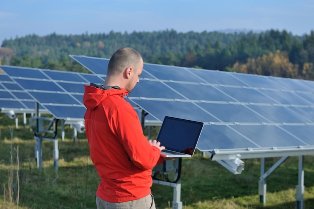 ingeniero de negocios que usa una computadora portátil en el campo de energía ecológica de la planta de paneles solares en segundo plano