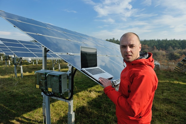 ingeniero de negocios que usa una computadora portátil en el campo de energía ecológica de la planta de paneles solares en segundo plano