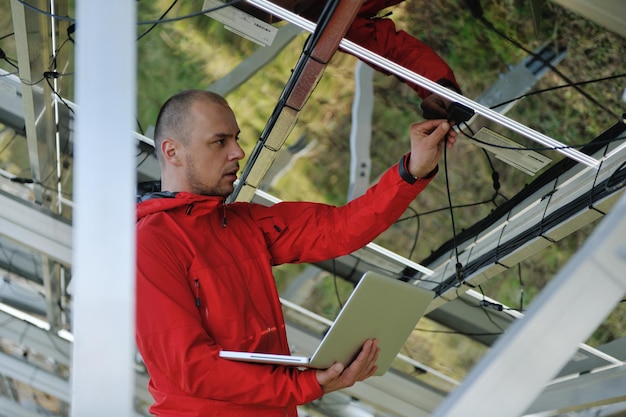 ingeniero de negocios que usa una computadora portátil en el campo de energía ecológica de la planta de paneles solares en segundo plano