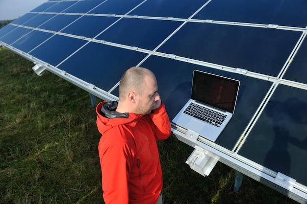 ingeniero de negocios que usa una computadora portátil en el campo de energía ecológica de la planta de paneles solares en segundo plano