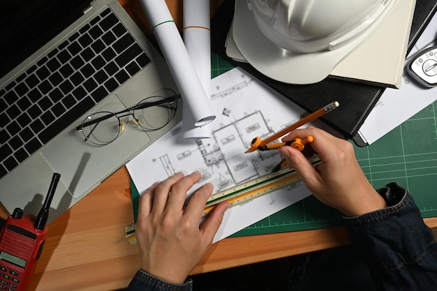 Ingeniero o arquitecto que trabaja con planos que planifican detalles de desarrollo en la estación de trabajo Vista superior