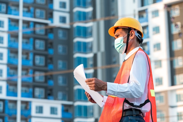 Foto ingeniero de pie para inspeccionar los planes de construcción en el sitio de construcción