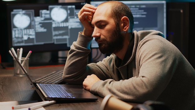 Ingeniero de programación que se queda dormido en el escritorio de la oficina, se siente cansado y trata de trabajar en el servidor de la base de datos. Desarrollador web agotado con sueño y bostezando tarde en la noche, computación en la nube.