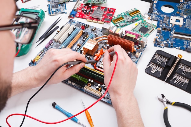 Ingeniero que controla la placa base con el multímetro de cerca. Diagnóstico informático, soporte de mantenimiento y concepto de servicio de reparación.