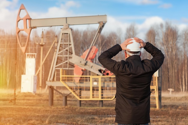 Un ingeniero químico con un casco blanco se agarró la cabeza con las manos mirando una bomba de aceite que producía petróleo crudo.