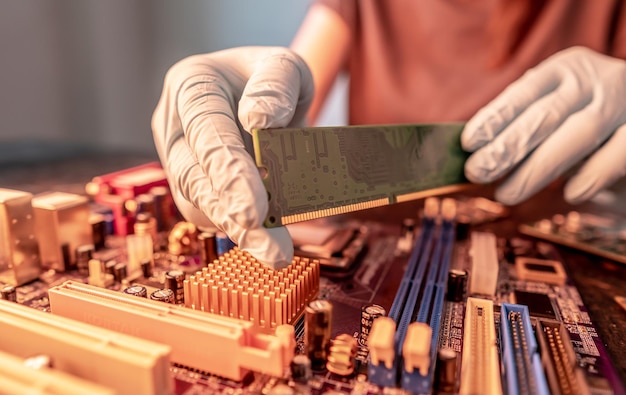 Un ingeniero de reparación sostiene un chip RAM con las manos e inserta la RAM en el zócalo de la placa base de la computadora