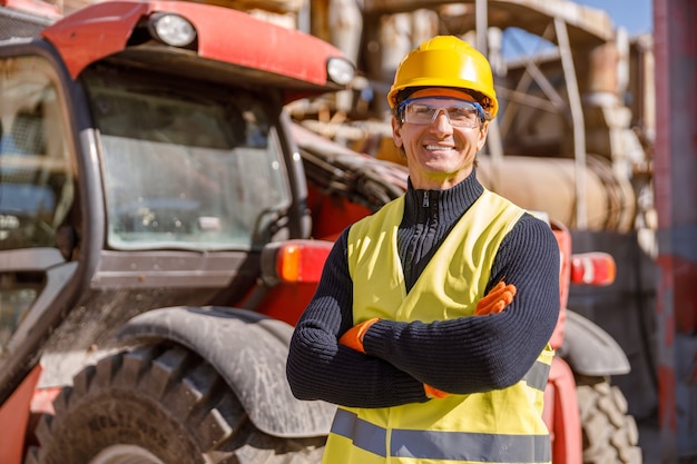 Ingeniero de sexo masculino alegre de pie por tractor en la fábrica.