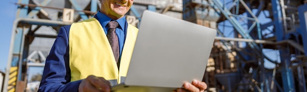 Ingeniero de sexo masculino alegre que usa la computadora portátil al aire libre en la fábrica