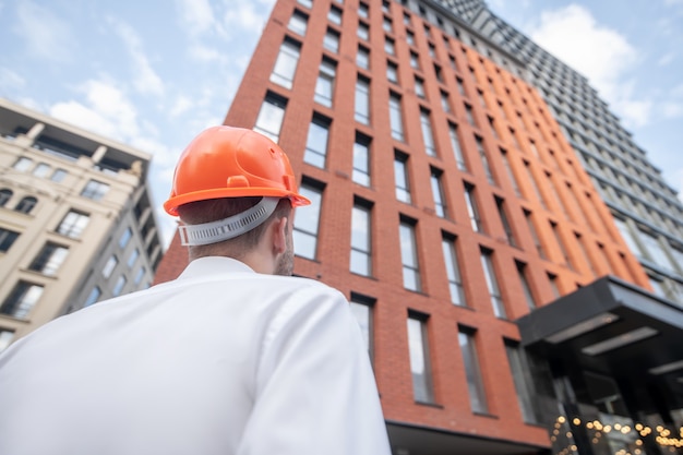 Ingeniero de sexo masculino en casco protector mirando el edificio