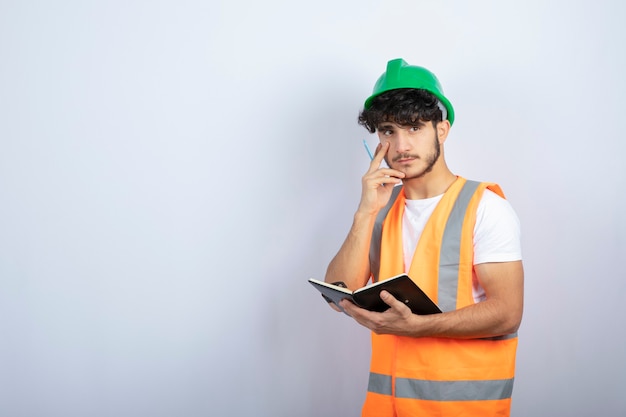 Ingeniero de sexo masculino guapo en casco verde con portátil sobre pared blanca. Foto de alta calidad