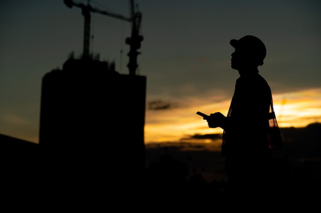 Ingeniero de sexo masculino que trabaja en el sitio de construcción en el momento de la puesta del sol silueta