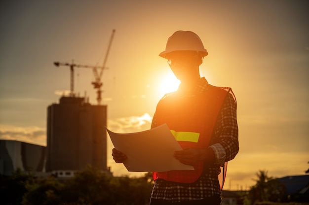 Ingeniero de sexo masculino que trabaja en el sitio de construcción en el momento de la puesta del sol silueta