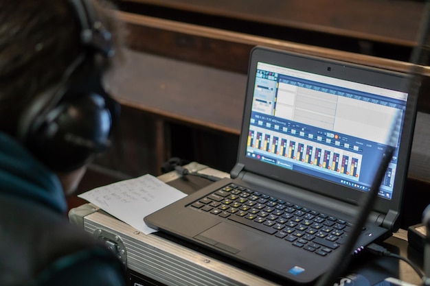 Un ingeniero de sonido con auriculares se sienta frente a una computadora portátil mientras graba o escucha Ingeniero de sonido masculino en un estudio de grabación