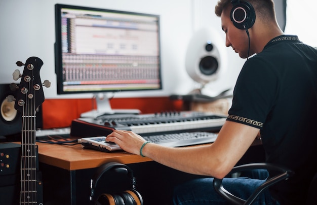 Foto ingeniero de sonido en auriculares trabajando y mezclando música en interiores en el estudio.