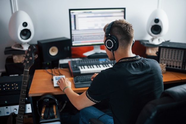 Foto ingeniero de sonido en auriculares trabajando y mezclando música en interiores en el estudio.
