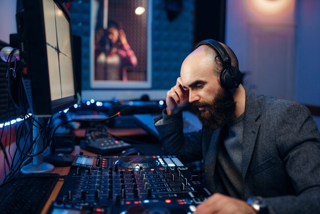 Ingeniero de sonido graba a cantante femenina en estudio.