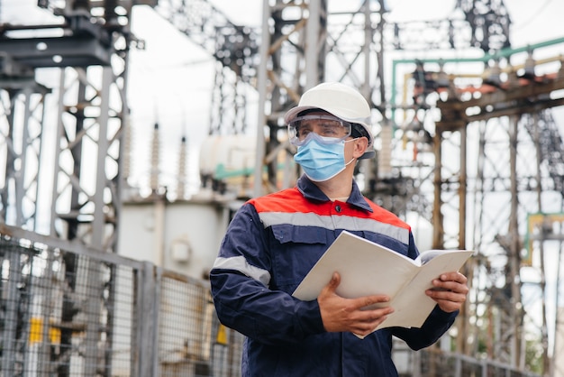 Un ingeniero de subestación eléctrica inspecciona equipos modernos de alto voltaje en una máscara en el momento de la pandemia