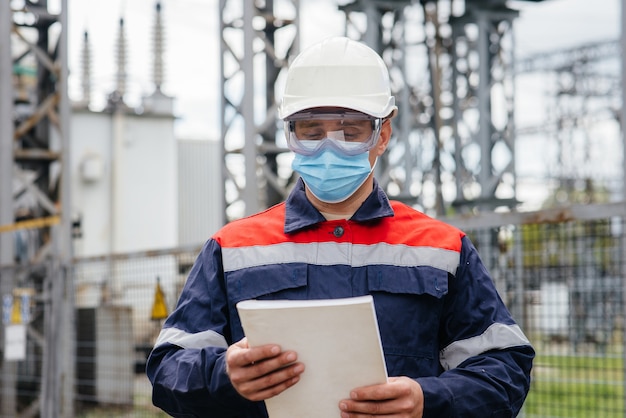 Un ingeniero de subestación eléctrica inspecciona equipos modernos de alto voltaje con una máscara en el momento de la pondemia. Energía. Industria.