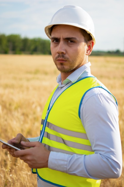 Un ingeniero con una tableta en las manos se encuentra en medio de un campo para controlar la cosecha.