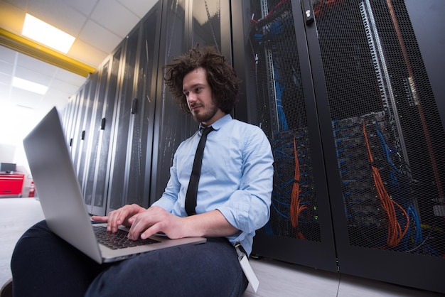 Ingeniero de TI masculino trabajando en una computadora portátil en la sala de servidores en un centro de datos moderno