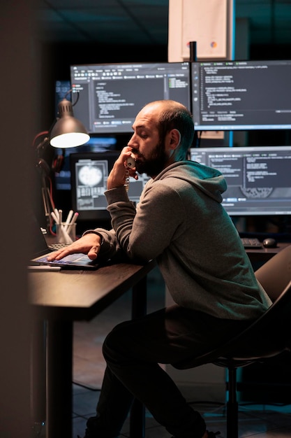 Ingeniero de TI que responde a una llamada de teléfono fijo en la oficina, hablando de codificar el script html en la línea telefónica del cable. Trabajar hasta altas horas de la noche para desarrollar un nuevo sistema informático y servidores de aplicaciones.