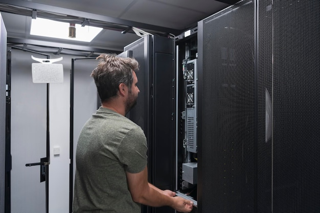 Ingeniero de TI que trabaja en la sala de servidores o en el centro de datos. El técnico coloca en un rack un nuevo servidor de una supercomputadora central de negocios corporativos o una granja minera de criptomonedas.