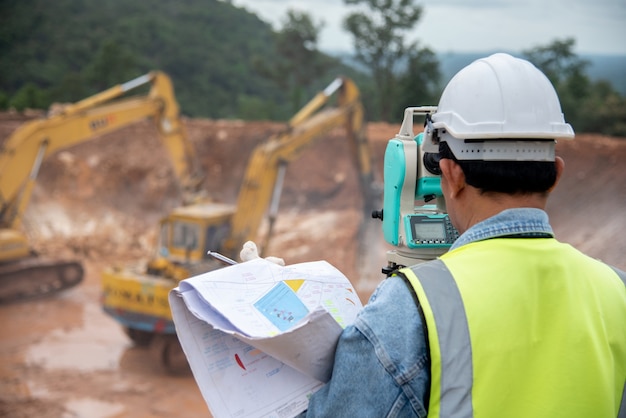 Ingeniero de topografía en sitio de construcción usa teodolito revisando trabajo de cimentación de excavación