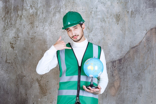 Ingeniero de uniforme amarillo y casco sosteniendo un globo terráqueo y pidiendo una llamada.