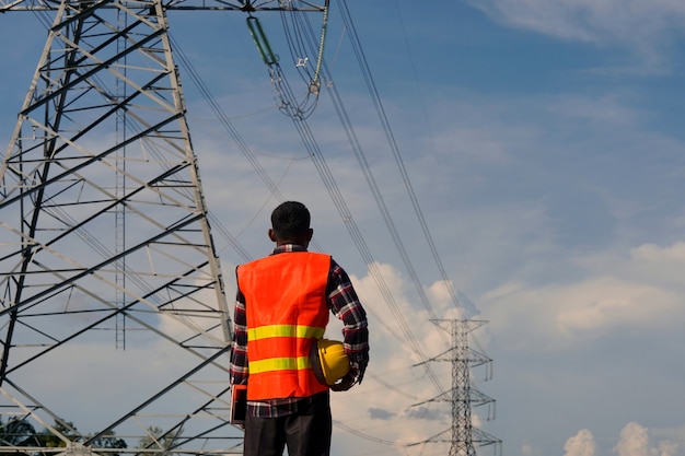 Un ingeniero usa una computadora portátil y está inspeccionando el trabajo de construcción. Un gran poste de energía eléctrica frente al sitio de construcción.