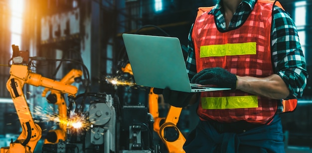 El ingeniero utiliza un software robótico avanzado para controlar el brazo robótico de la industria en la fábrica.