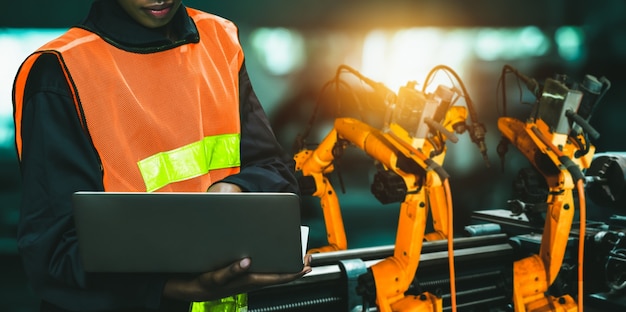 El ingeniero utiliza un software robótico avanzado para controlar el brazo robótico de la industria en la fábrica.