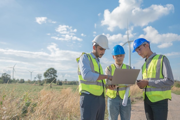 Ingenieros asiáticos que trabajan en el trabajo de campo al aire libre Trabajadores que caminan e inspeccionan la construcción y la máquina alrededor del sitio del proyecto Turbina eólica eléctrica de energía de recursos limpios y medio ambiente sostenible