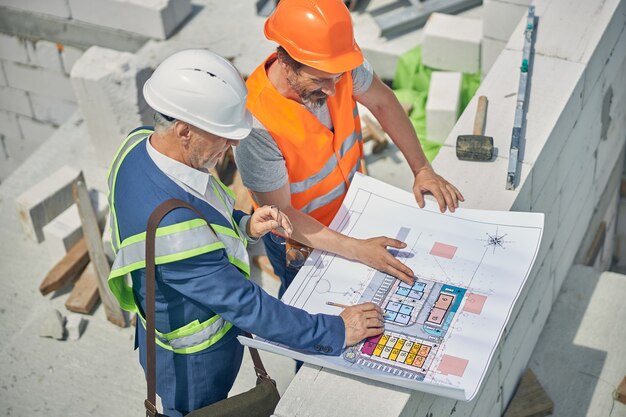 Ingenieros caucásicos en chalecos reflectantes y cascos discutiendo un plan de casa