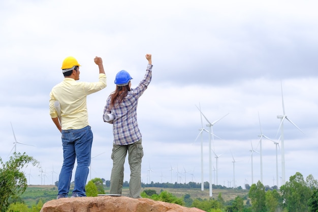 Los ingenieros están de pie sosteniendo planos y felicitan los proyectos de turbinas eólicas para generar electricidad y verificar la dirección del viento.