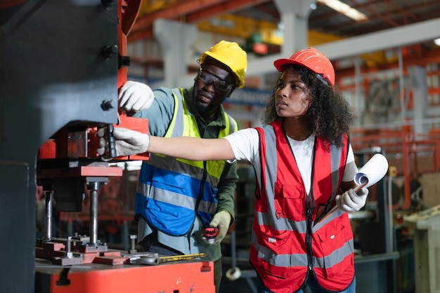 Ingenieros femeninos y masculinos en chalecos de seguridad revisando y reparando máquinas en fábrica