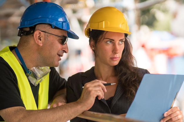 Foto ingenieros y ingenieras en el sitio de construcción revisando planos y planos de la oficina