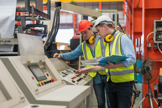 Ingenieros masculinos en chaleco de seguridad con casco discutiendo mientras revisan y reparan la máquina en la fábrica