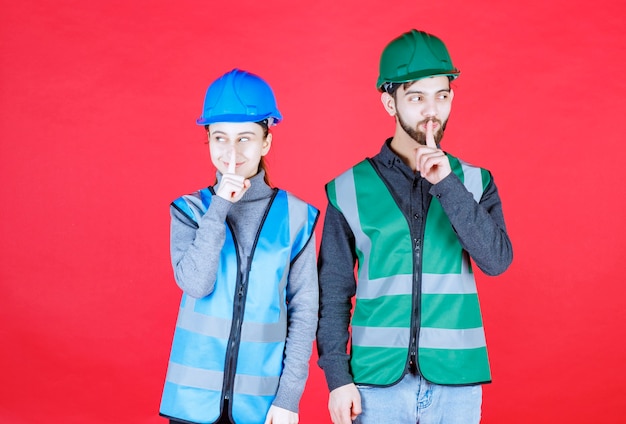 Ingenieros masculinos y femeninos con casco y equipo pidiendo silencio.