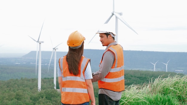 Ingenieros masculinos y femeninos que trabajan en un parque eólico en la cima de una colina o montaña en el ideal rural progresivo para la producción futura de energía sostenible renovable