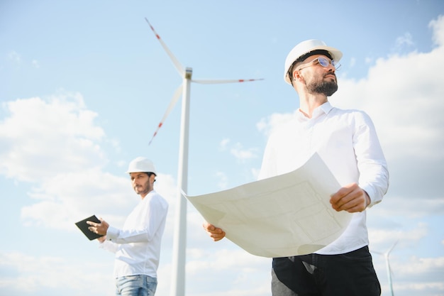 Ingenieros masculinos indios y europeos que trabajan en un parque eólico con molinos de viento